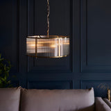 Rothbury 3 Light Pendant in antique brass with ribbed glass panels, hung on a chain above a sofa against dark panelled walls.