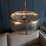 Rothbury 3 Light Pendant in antique brass with ribbed glass panel shades, hung on a chain above a beige sofa in a living room setting.