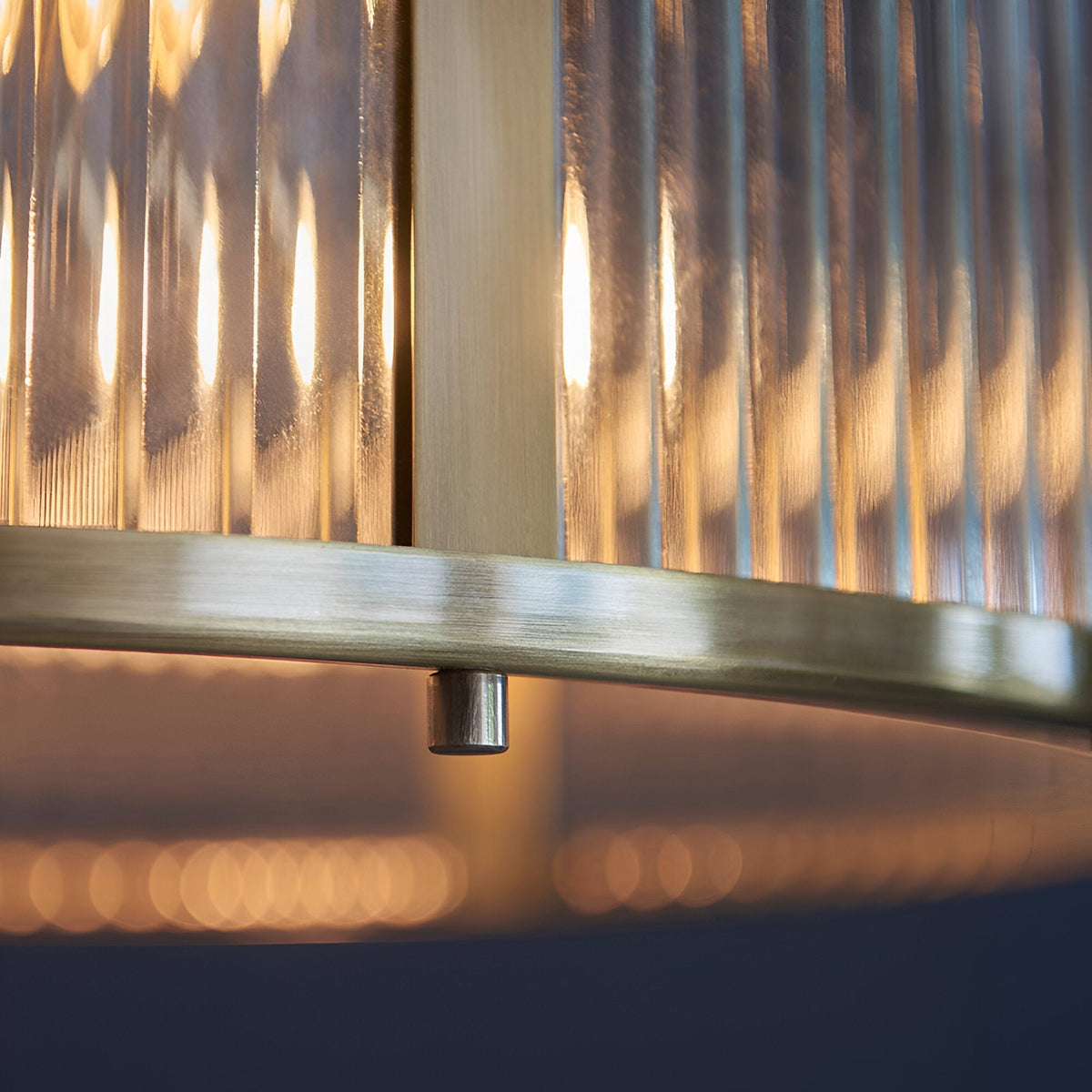 Close-up of the Rothbury 3 Light Pendant, showing ribbed glass shade panels and antique brass frame with lit bulbs glowing within.