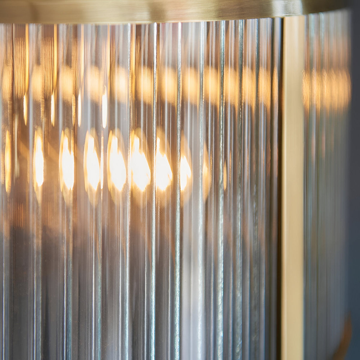 Rothbury 3 Light Pendant in antique brass, close-up of ribbed glass shades glowing warmly around a brass frame edge.