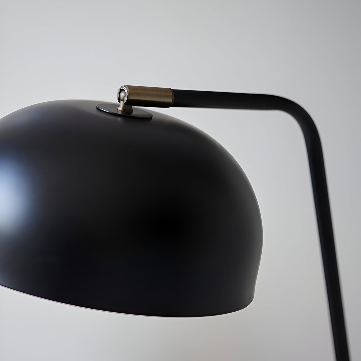 Close-up of the Ashdon Table Lamp's matt black dome shade with antique brass pivot joint and angled arm, set against a plain light background.