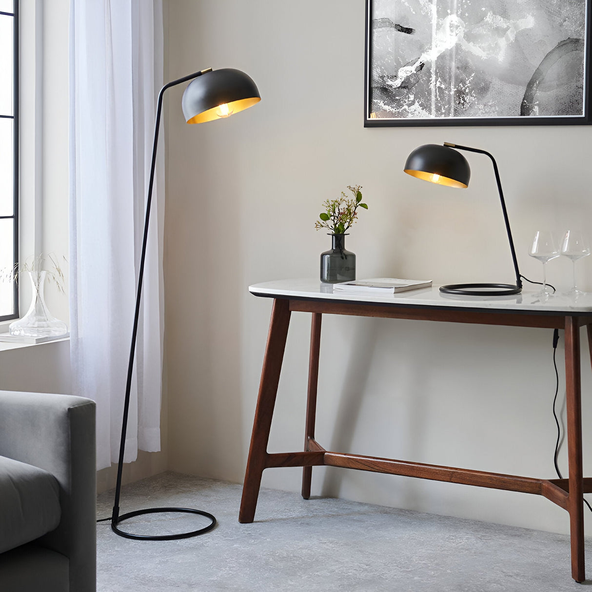 Ashdon Table Lamp in matt black with antique brass inner shade and adjustable head, shown on a console table beside a floor lamp in a living room.
