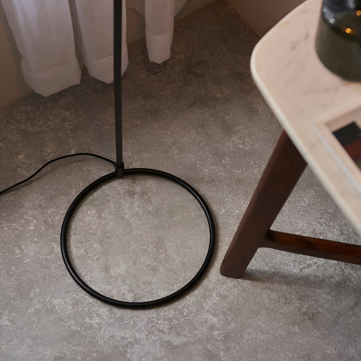 Close-up of the Endon Ashdon floor lamp's matt black circular base and slim stem on stone flooring beside a marble-topped wooden side table.