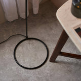 Close-up of the Endon Ashdon floor lamp's matt black circular base and slim stem on stone flooring beside a marble-topped wooden side table.