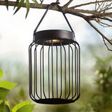 Endon Cranwood LED solar table lamp in matt black, open metal cage design with leather strap handle, hung from a tree branch in a garden setting.