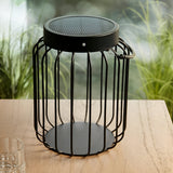 Endon Cranwood LED solar table lamp in matt black with open metal cage frame and hanging handle, shown on a wooden garden table beside grasses.