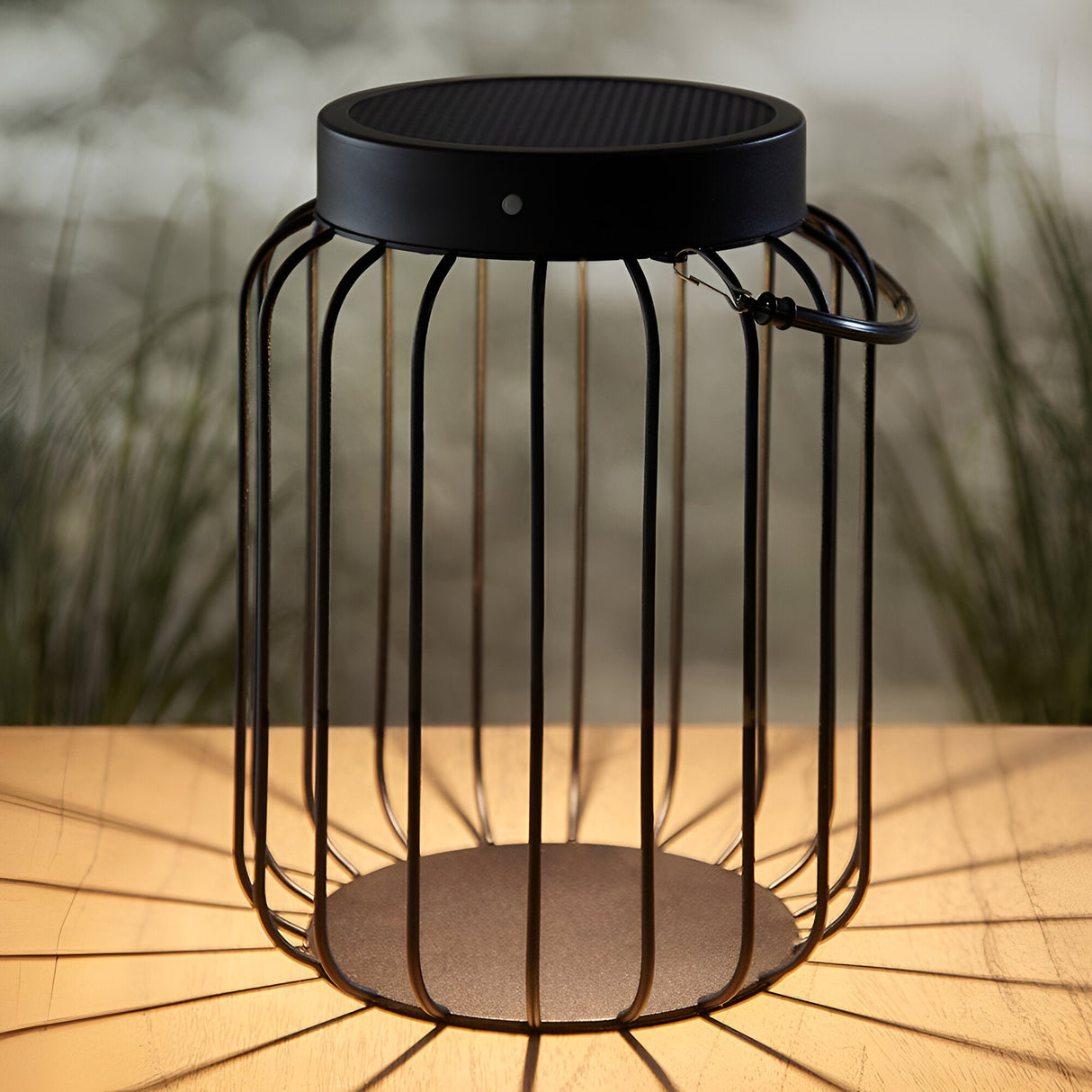Endon Cranwood solar LED table lamp in matt black with open metal cage frame and carabiner handle, shown on an outdoor wooden table.