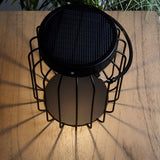 Top-down view of the Endon Cranwood LED solar table lamp in matt black, with caged metal frame and solar panel, on a wooden garden table.