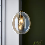 Brockmere Pendant in Brass & Gold, a single-light fixture with an oval champagne lustre glass shade and satin brass fitting, lit against a dark green wall.