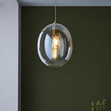 Brockmere Pendant in Brass & Gold, an oval champagne lustre glass shade with satin brass fitting and E27 bulb, shown hanging against a dark green wall.