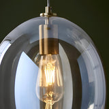 Close-up of the Brockmere Pendant in brass and gold, showing an oval champagne lustre glass shade with satin brass fitting and lit E27 bulb.