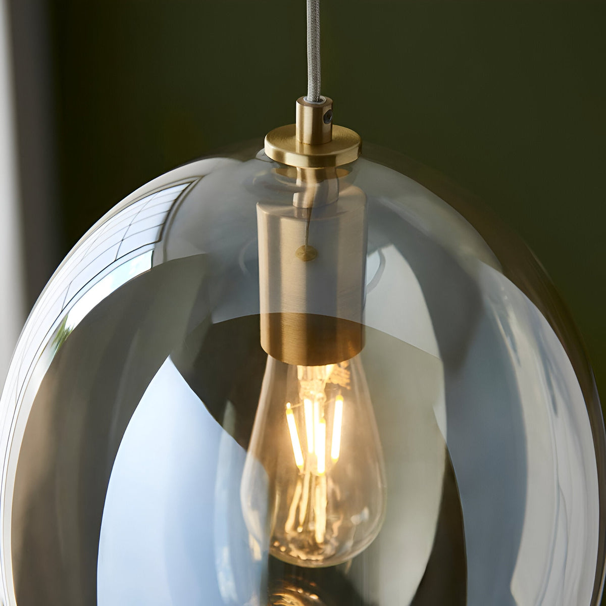 Close-up of the Brockmere Pendant's satin brass fitting and E27 bulb inside an oval champagne lustre glass shade with warm reflections.