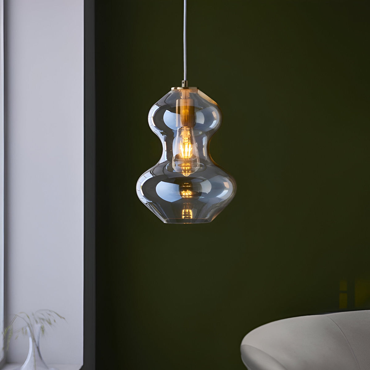 Brockley Pendant in champagne lustre glass with satin brass fitting, curved shade glowing with a warm E27 bulb against a dark green wall.