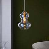 Brockley Pendant in champagne lustre glass with satin brass fitting, curved shade glowing with a warm E27 bulb against a dark green wall.