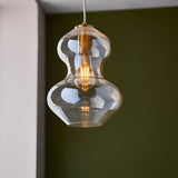 Brockley Pendant in champagne lustre glass with a curved double-bubble shade and satin brass fitting, shown lit against a dark green wall.