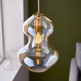 Brockley Pendant in champagne lustre glass with a curved shape and satin brass fitting, shown lit with an E27 bulb against a green wall.