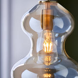 Brockley Pendant in satin brass with a curved champagne lustre glass shade, close-up showing the E27 bulb glowing inside.