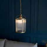 Endon Caldcombe pendant with ribbed glass shade and antique brass frame on chain suspension, shown against a dark blue panelled wall above a grey sofa.