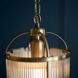 Close-up of the Endon Caldcombe pendant showing its antique brass frame, ribbed glass shade, and chain suspension against a dark blue background.