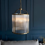 Endon Caldcombe 4 light pendant in antique brass with clear ribbed glass cylindrical shade and chain suspension, shown against a dark blue panelled wall.