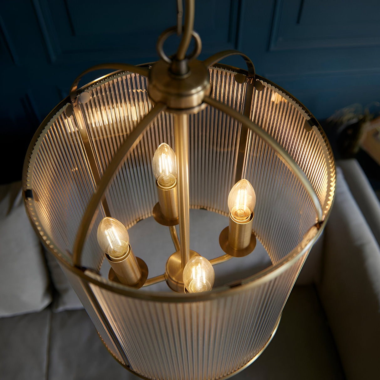 Endon Caldcombe 4 light pendant illuminated from below, showing four E14 candle bulbs within a ribbed glass and antique brass frame against a blue wall.