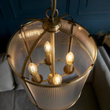 Endon Caldcombe 4 light pendant illuminated from below, showing four E14 candle bulbs within a ribbed glass and antique brass frame against a blue wall.