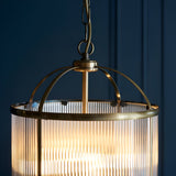 Close-up of Endon Caldcombe 4 light pendant showing antique brass domed frame, ribbed glass shade and chain suspension against a dark blue panelled wall.