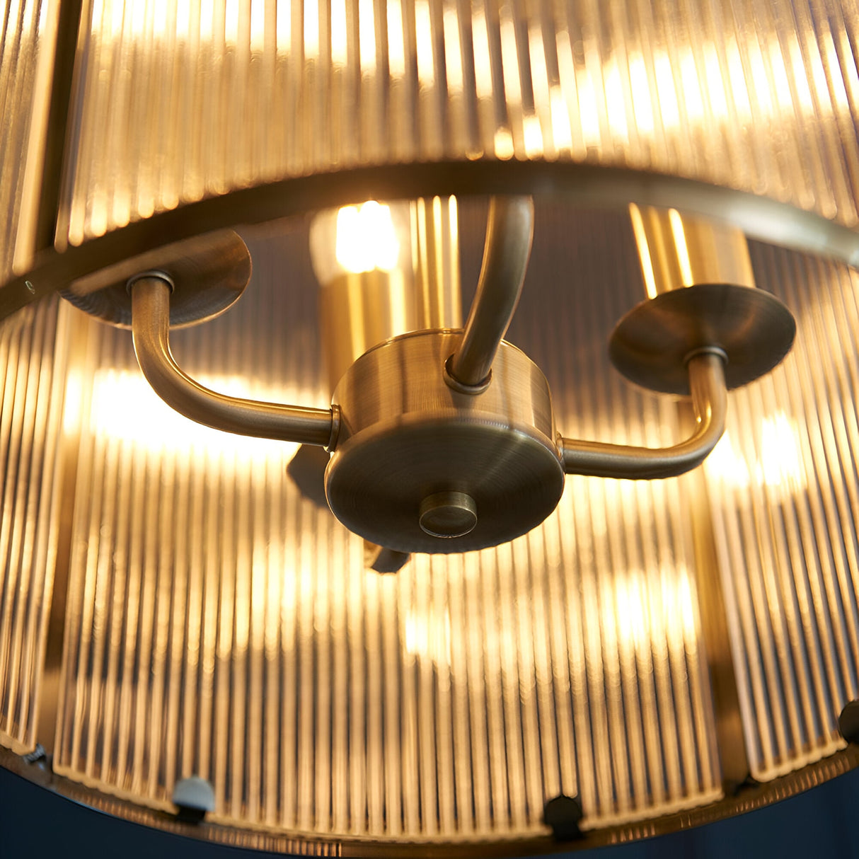 Close-up of the Endon Caldcombe 4 Light Pendant showing antique brass arms, central hub and illuminated E14 lamps behind ribbed glass shades.