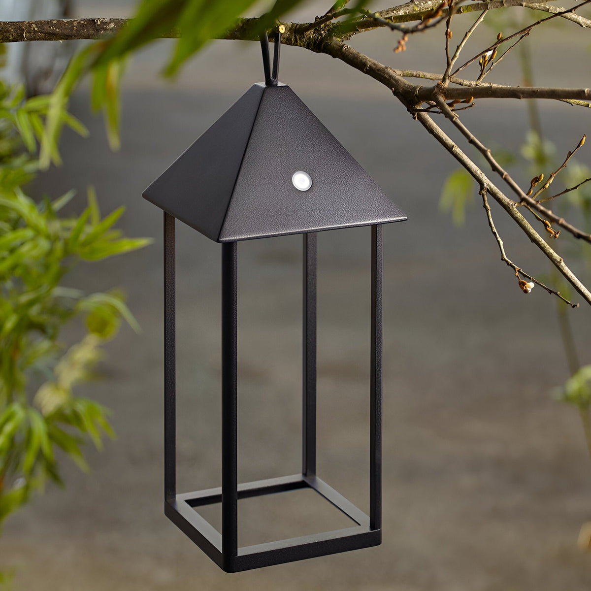 Endon Brenmont large matt black aluminium lantern table lamp with pyramid top and open frame, hanging from a tree branch outdoors.