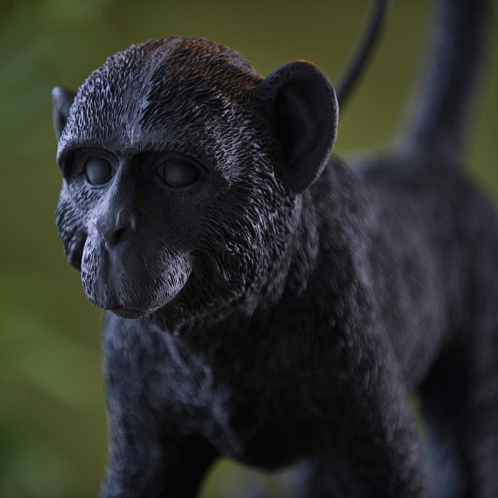 Belvoir Table Lamp in black – close-up of the resin monkey figure base, showing detailed fur texture and finish against a blurred green background.