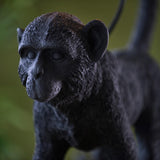 Belvoir Table Lamp in black – close-up of the resin monkey figure base, showing detailed fur texture and finish against a blurred green background.