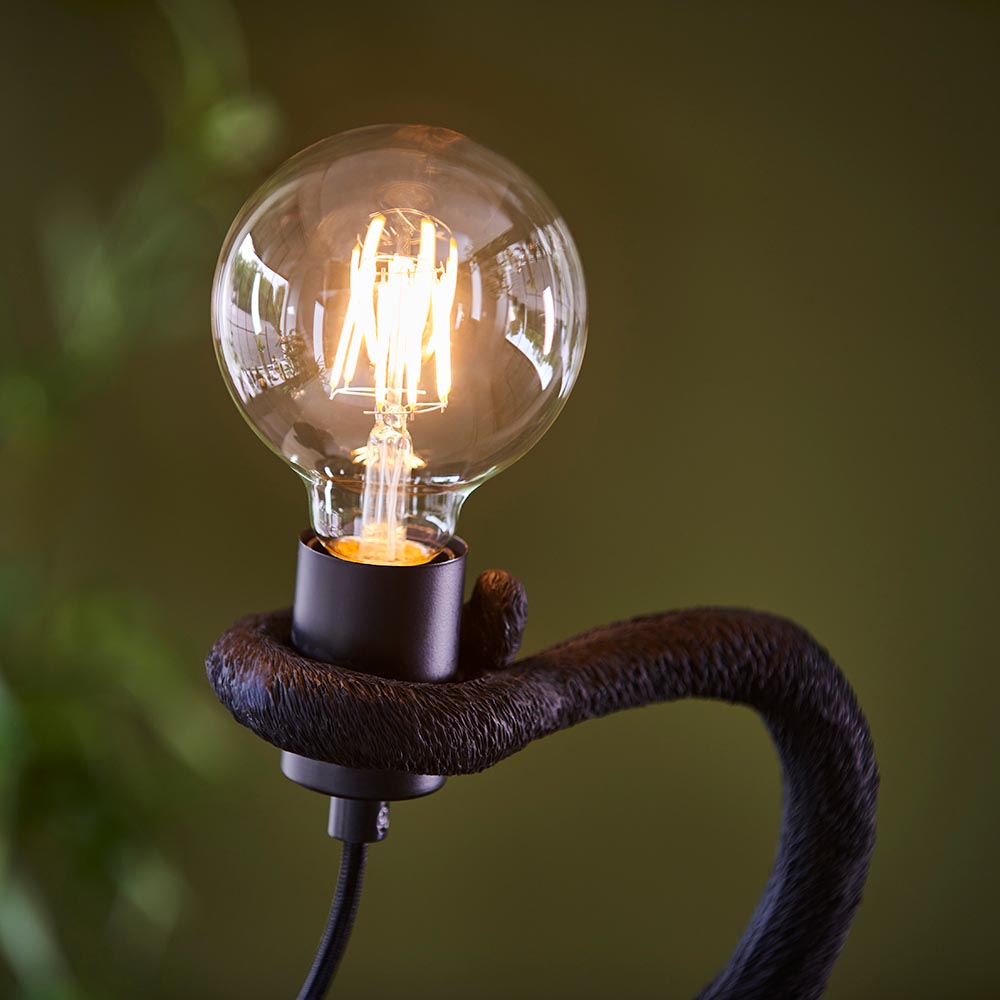 Belvoir Table Lamp in matt black resin, monkey-shaped base holding an exposed filament globe bulb, inline switch visible.