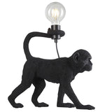 Belvoir Table Lamp in black, a resin monkey figure holding an exposed filament bulb aloft, shown on a plain white background.