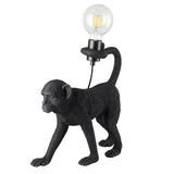 Belvoir Table Lamp in matt black resin, shaped as a walking monkey with tail raised to hold an exposed filament bulb, on a plain white background.