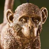 Close-up of the Endon Belvoir table lamp showing the detailed resin monkey face in a warm vintage gold finish against a soft green background.