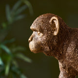 Endon Belvoir table lamp in gold, close-up profile of the detailed resin monkey figurine's head against a blurred green foliage background.
