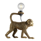 Endon Belvoir table lamp shaped as a walking gold resin monkey holding an exposed filament bulb with its tail, shown on a white background.