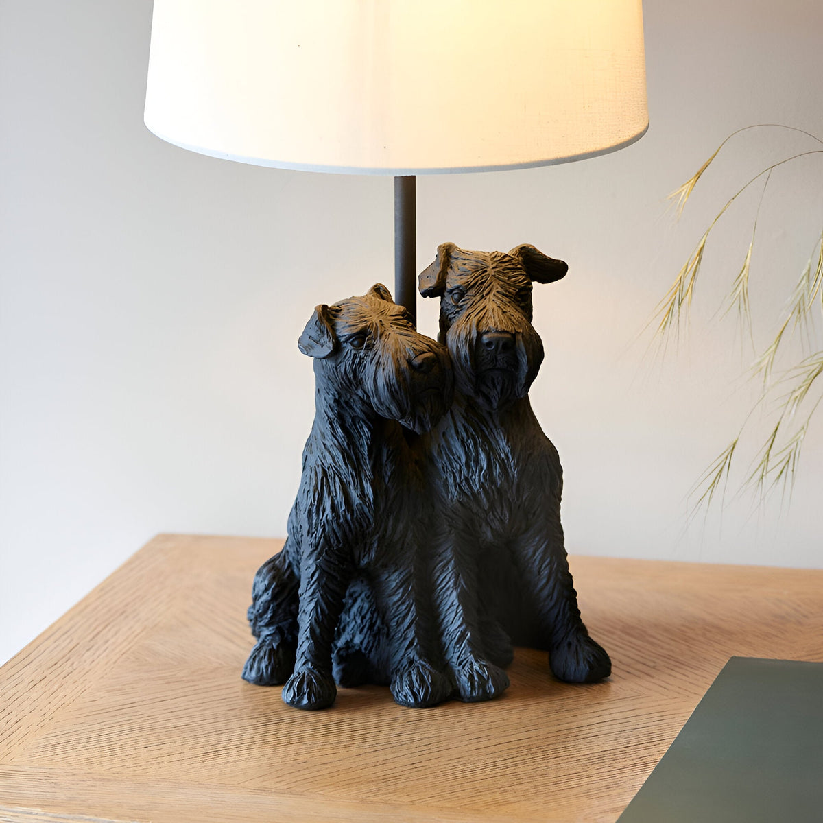 Danegrove Table Lamp in matt black resin, featuring a detailed two-dog figure base and cream fabric shade, shown on a wooden sideboard.