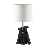 Danegrove Table Lamp in matt black resin, featuring two seated dogs at the base and a cream fabric drum shade, on a plain white background.