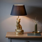 Endon Brambury table lamp with a vintage gold resin fox base and black tapered fabric shade, lit on a wooden console beside a brass vase.