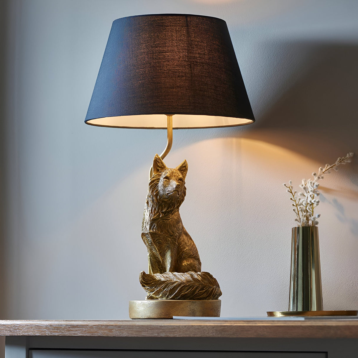 Endon Brambury table lamp with a vintage gold resin fox base and black tapered fabric shade, styled on a wooden console beside a brass vase.