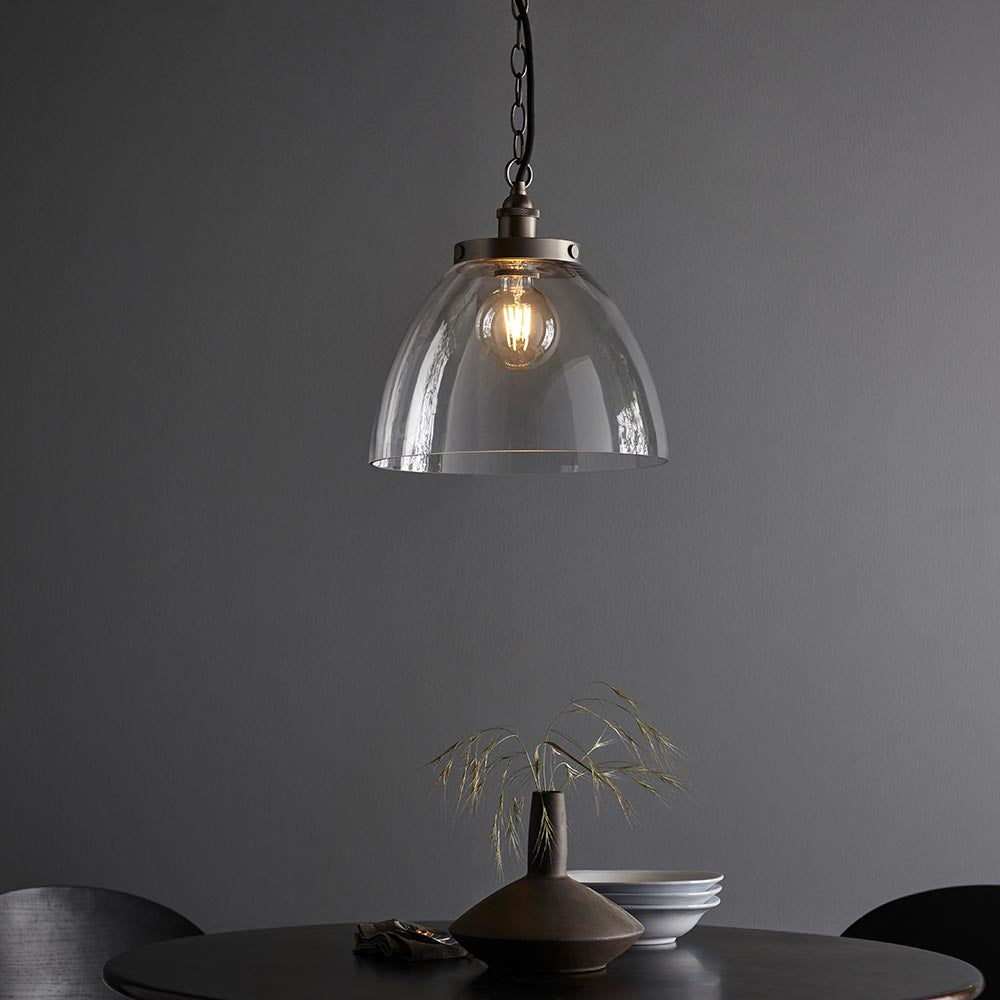 Wentworth Pendant in silver with clear glass dome shade and exposed filament bulb, hung on a black chain above a dining table.