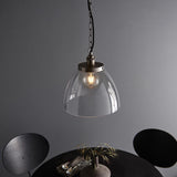 Wentworth Pendant in silver, industrial-style clear glass dome shade with knurled lampholder and filament bulb, hung on a black chain above a dark dining table.