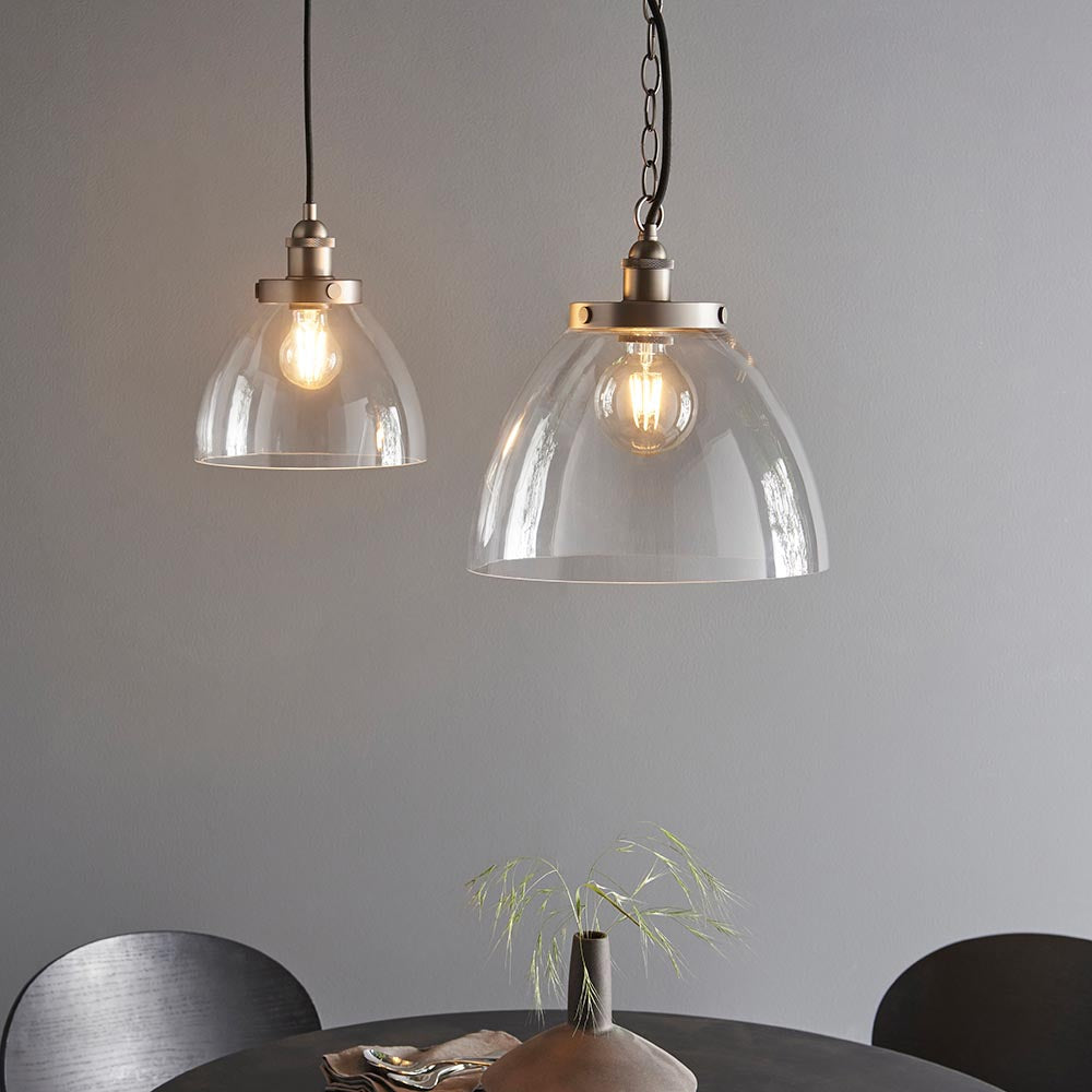 Wentworth Pendant in silver, two clear glass dome shades with brushed silver knurled lampholders on chain suspension, shown lit above a dining table.