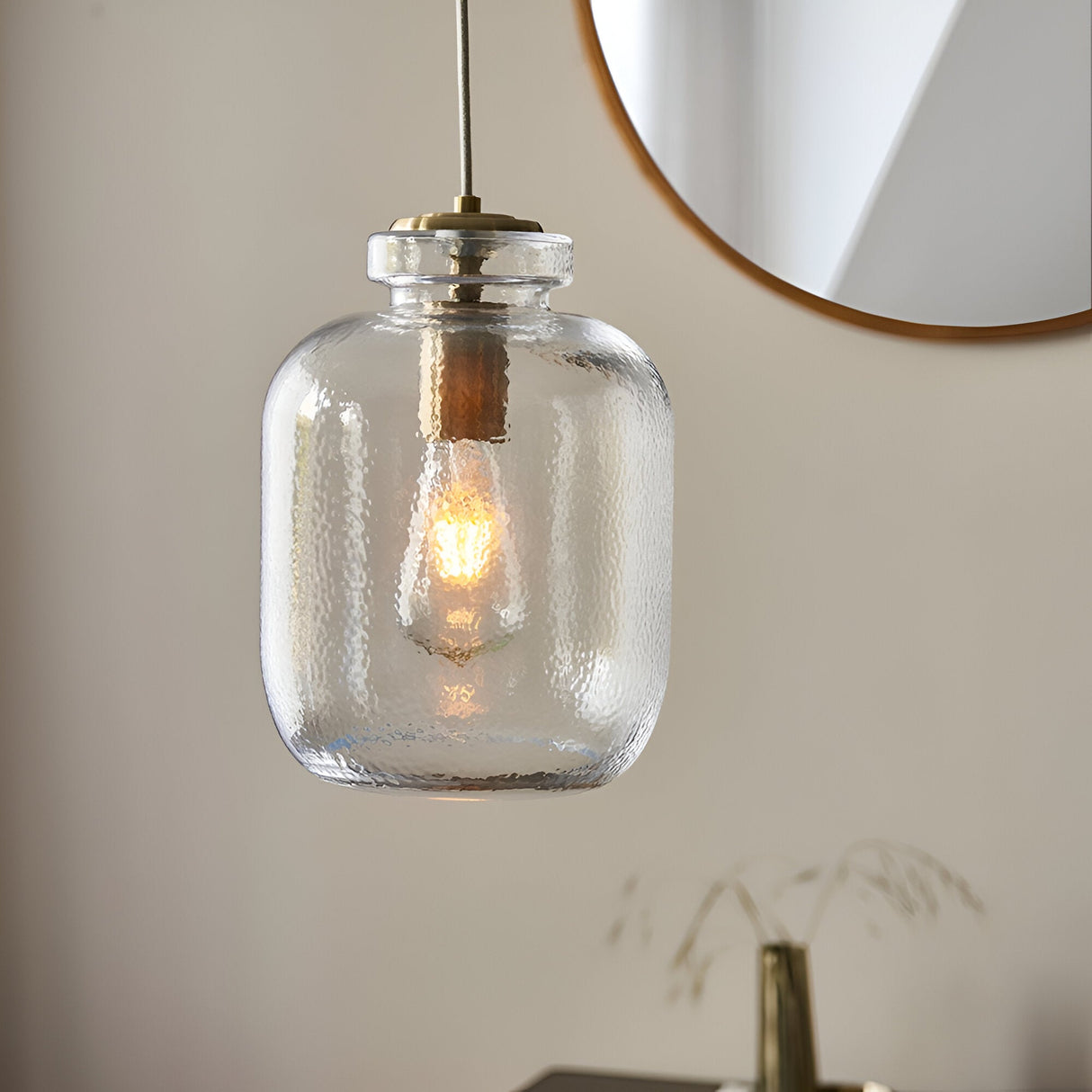 Caldwood Pendant in brass and natural finish, textured clear glass shade with exposed bulb, hung near a round mirror in a living space.