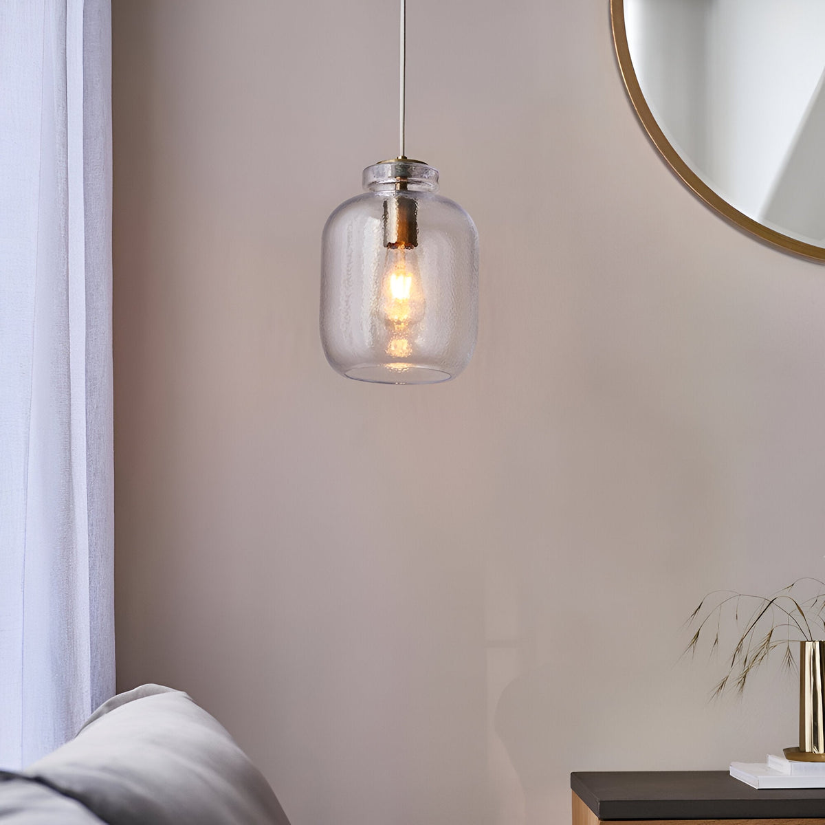 Caldwood Pendant in brass and natural finish, single-light fixture with textured clear glass shade and lit bulb, hung in a living room near a round mirror.