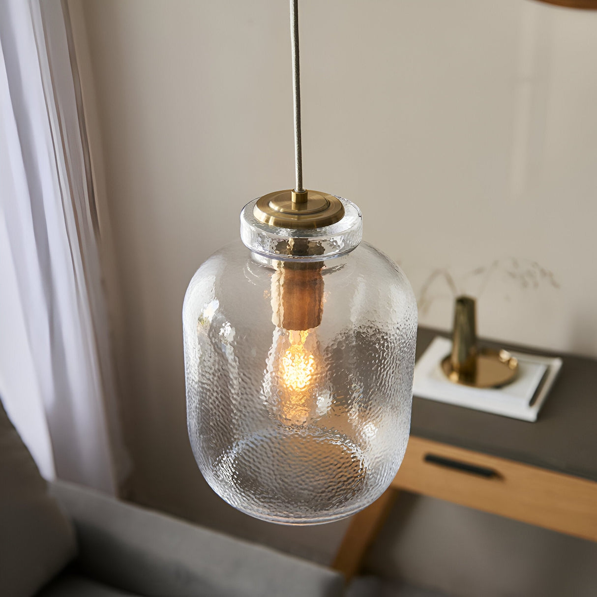 Caldwood Pendant in Brass & Natural, a single-light fixture with textured clear glass shade and antique brass fittings, shown hanging in a living room setting.
