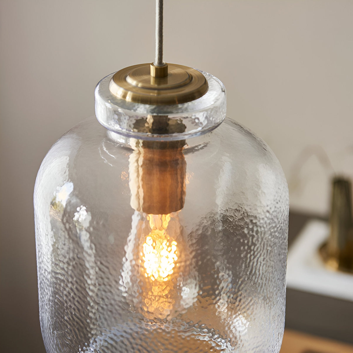 Caldwood Pendant close-up showing textured clear glass shade, antique brass fitting, and lit E27 bulb inside.