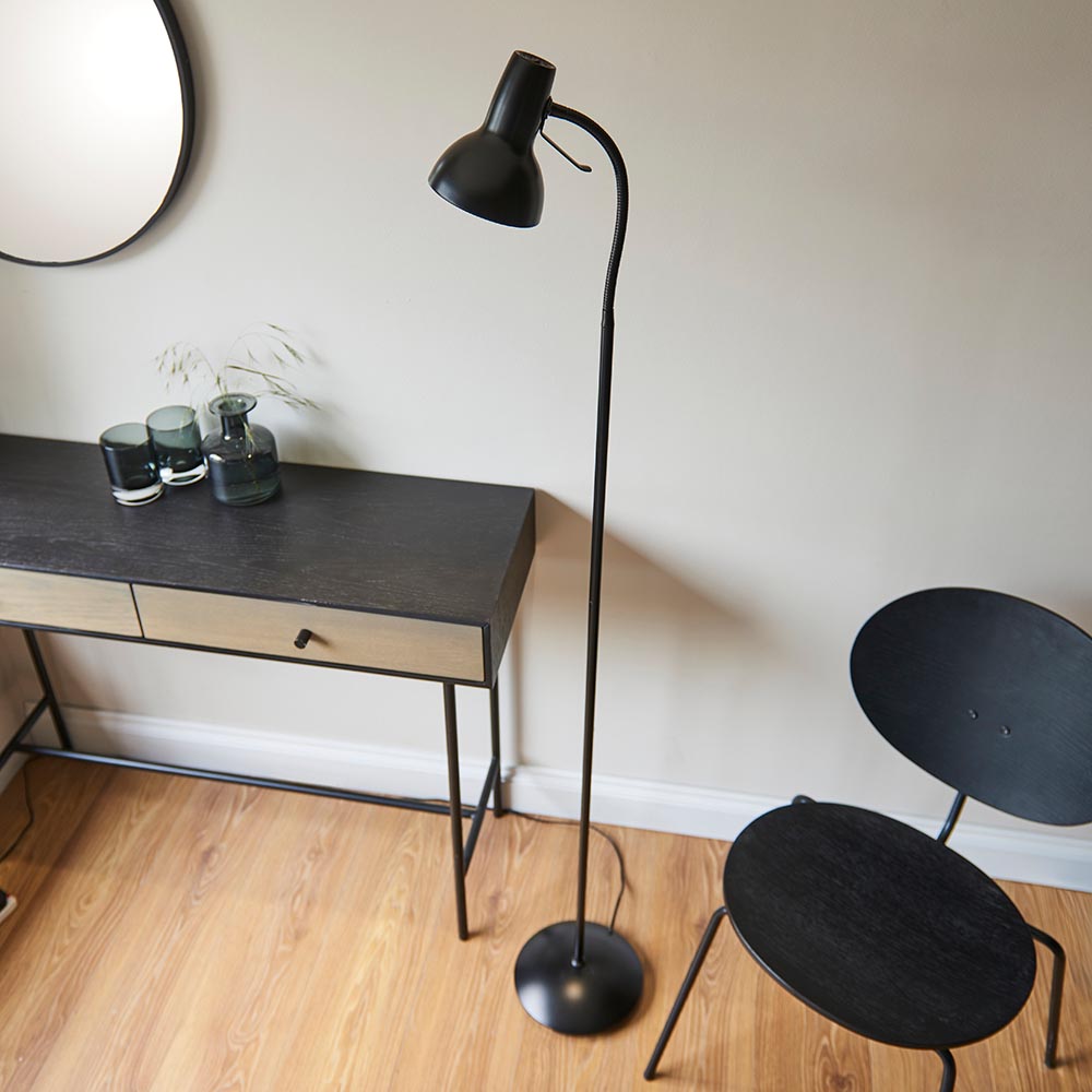Endon Alderton floor lamp in matt black with adjustable head, curved handle and round base, beside a dark console table and chair in a living room.