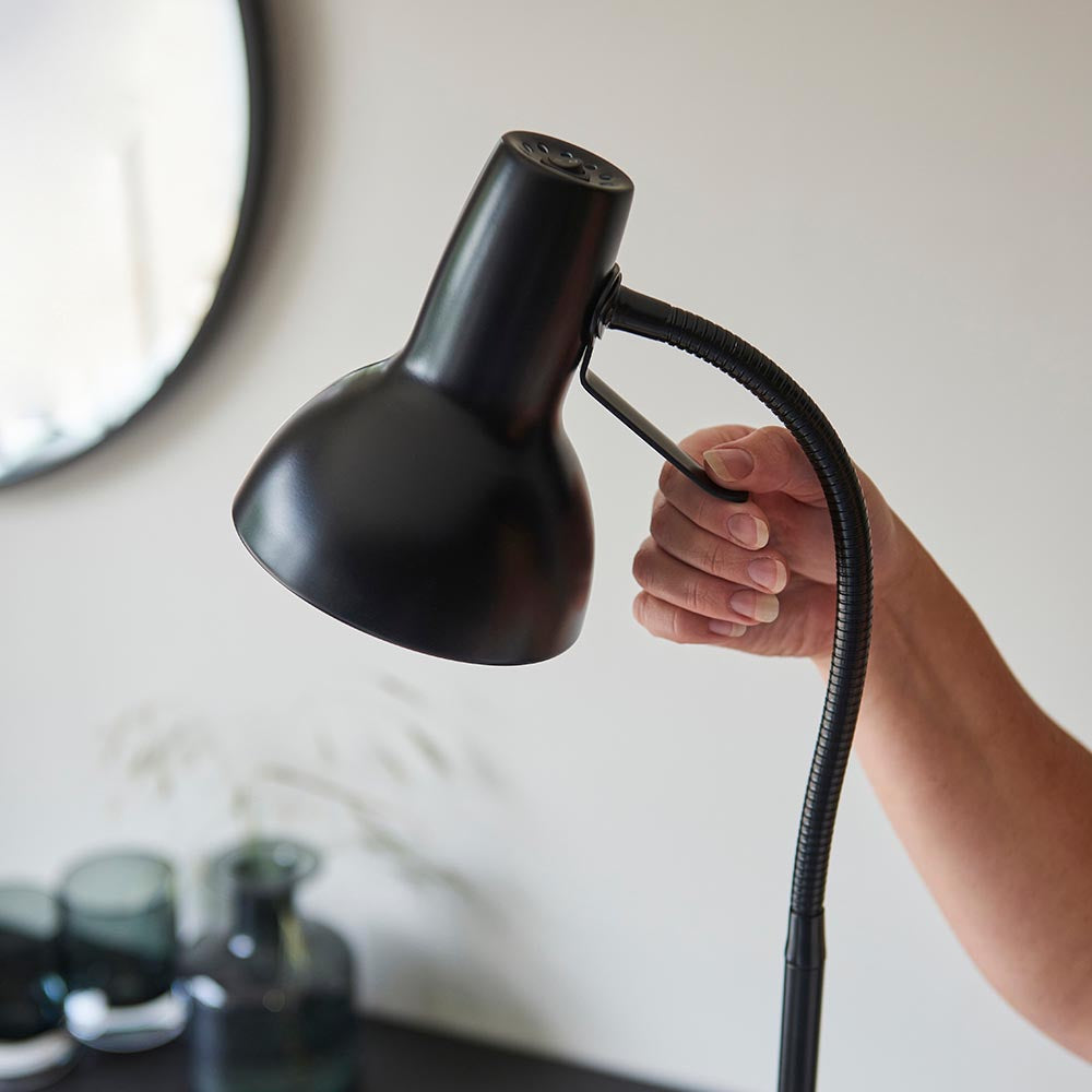Hand adjusting the matt black head of the Endon Alderton floor lamp by its curved handle, with a flexible gooseneck stem and round shade.